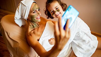 Eine Mutter mit ihrem Kind bei einer Gesichtsbehandlung und machen ein Selfie mit dem Handy im Familienhotel Das Bayrischzell in Oberbayern