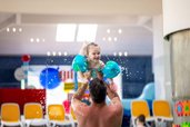 Badespaß im Familienhotel Ungarn: Ein Vater hebt sein lachendes Kleinkind spielerisch im Wasser hoch – unvergessliche Familienmomente im Kolping Family Resort.