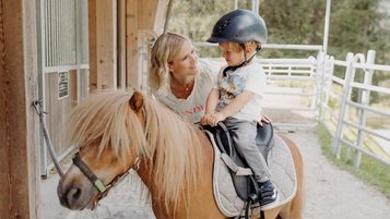 Kleiner Junge sitzt auf einem Pony im Reitstall des Habachklause Familien Bauernhof Resorts im Salzburger Land.