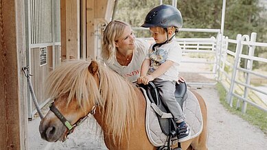 Kleiner Junge sitzt auf einem Pony im Reitstall des Habachklause Familien Bauernhof Resorts im Salzburger Land.