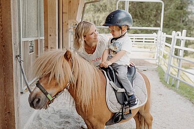 Kleiner Junge sitzt auf einem Pony im Reitstall des Habachklause Familien Bauernhof Resorts im Salzburger Land.