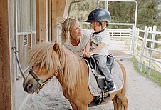 Kleiner Junge sitzt auf einem Pony im Reitstall des Habachklause Familien Bauernhof Resorts im Salzburger Land.