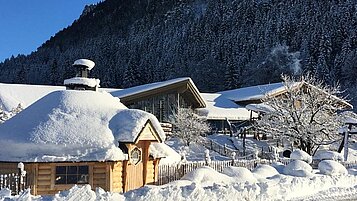 Hotelansicht des Spa- & Familien-Resorts Krone im Winter. Die Dächer befinden sich unter einer Schneeschicht und auch der umliegende Garten ist weiß bedeckt.