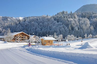 Blick auf die tief verschneite Winterlandschaft rund um das Familienhotel Landgut Furtherwirt in Tirol mit Langlaufloipe und Kinder-Skihang 