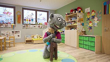 Das Kind umarmt in der Kinderbetreuung das Maskottchen des Familienhotels Das Bayrischzell in Bayern.