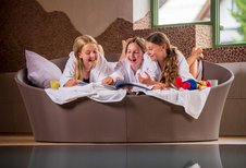 Drei Kinder im Bademantel liegen lachend auf einer Relaxliege im Familienhotel Furtherwirt am Pool.