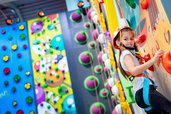 Bunte Kletterwelt im Familienhotel Ungarn: Ein Mädchen erklimmt strahlend die spaßige Indoor-Kletterwand im Kolping Family Resort – Abenteuer für kleine Gipfelstürmer.