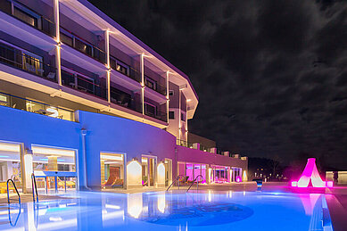 Außenansicht vom Pool mit Ambientebeleuchtung am Abend im Familienhotel Aigo welcome family in Oberösterreich