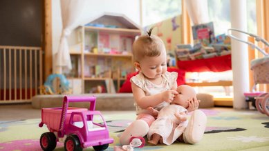 Kleines Kind spielt liebevoll mit einer Puppe in der Babybetreuung im Familienhotel Alpenhotel Kindl.