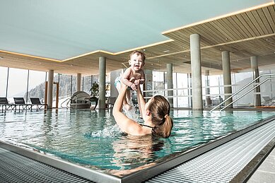 Eine Mutter hebt ihr Kind in die Höhe im Indoorpool im Almfamilyhotel Scherer in Tirol