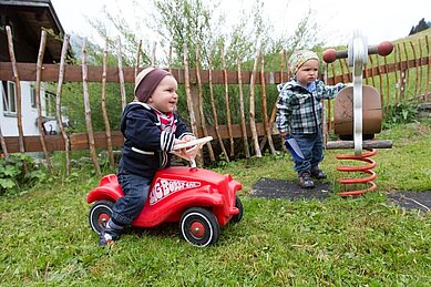 Ein Kind sitzt auf einem Bobbycar im Aussenbereich des Familienhotels Alphotel