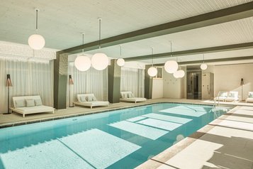 Indoor-Pool mit Ruheliegen rundherum im Familienhotel Engel Gourmet & Spa