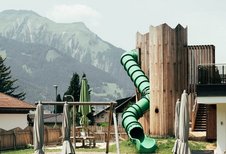 Der Blick vom Poolbereich auf den Abenteuerspielplatz mit großer Röhrenrutsche im Familienhotel Tirolerhof