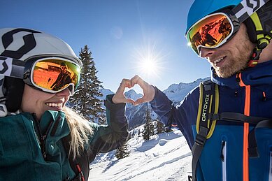 Eltern posieren auf den verschneiten Bergen für das Galtenberg Family & Wellness Resort in Tirol.