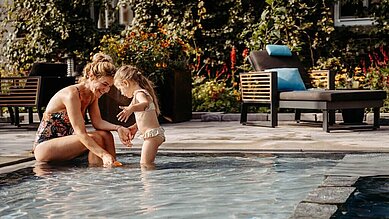 Mutter planscht gemeinsam mit ihrer Tochter im Kinderbecken des Außenpools im Familienhotel Landhaus Averbeck in der Lüneburger Heide.