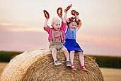 Kinder sitzen in Tracht auf einem Heuballen und halten Brezen in die Luft im Familienhotel Bavaria im Allgäu.