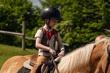 Junge sitzt auf einem Pferd beim Reitunterricht im Bernsteinreiter Schlossresort