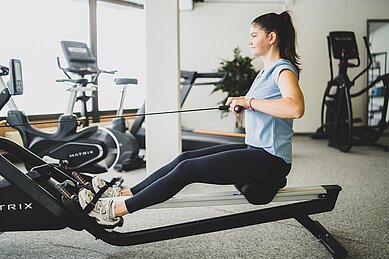 Eine Frau trainiert auf einem Rudergerät im Fitnessstudio im Familienhotel Gorfion in Liechtenstein