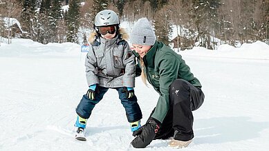 Kleiner Junge lernt im Familienhotel Post Family Resort Skifahren, die Skilehrerin unterstützt ihn dabei im Familienhotel Post Family Resort.