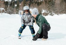 Kleiner Junge lernt im Familienhotel Post Family Resort Skifahren, die Skilehrerin unterstützt ihn dabei im Familienhotel Post Family Resort.