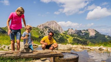 Eine Familie genießt das Spielen am erfrischenden Wasserspielplatz inmitten traumhafter Bergkulisse in Kärnten