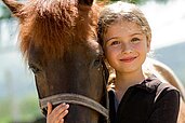 Mädchen kuschelt mit einem Pferd auf dem Pferdehof des Bernsteinreiter Schlossresorts