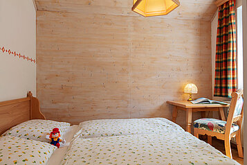 Schönes Doppelbett im Familienzimmer mit einem kleinen Tisch und großem Fenster im Familienhotel Kinderhotel Bruckwirt in Oberösterreich.