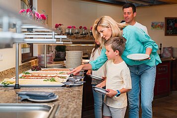 Mutter und Sohn bedienen sich am ausgiebigen Frühstücksbuffet im Familienhotel Das Hopfgarten