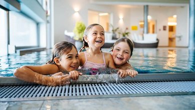Drei lachende Kinder spielen gemeinsam im Indoor-Pool des Familien Resort Petschnighof in Kärnten.