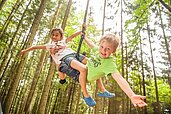 Zwei Kinder schwingen im Wald an einem Seil am Baum im Urlaub im Landhaus zur Ohe im bayerischen Wald.