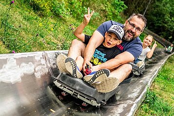 Eine Familie fährt eine Sommerrodelbahn in der Nähe des Familienhotels Rhön Feeling hinab.