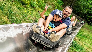 Eine Familie fährt eine Sommerrodelbahn in der Nähe des Familienhotels Rhön Feeling hinab.