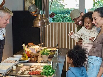 Eine Familien mit zwei Kindern steht am Buffet und betrachtet die Speisenauswahl.