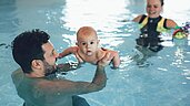 Eltern schwimmen mit ihrem Baby im Familienhotel Post Family Resort im Salzburger Land.