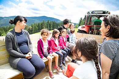 Kinder sitzen auf dem Hänger hinter dem Trecker und fahren zum Hotel im Familienhotel Der Ponyhof Steiermark.