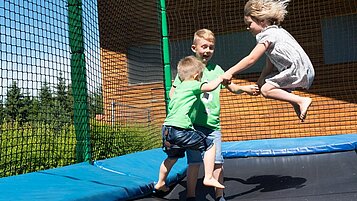 Kinder springen fröhlich auf dem Outdoor-Trampolin im Waldspielplatz im Familienhotel Ulrichshof im Bayerischen Wald