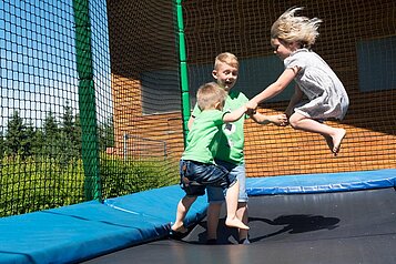 Kinder springen fröhlich auf dem Outdoor-Trampolin im Waldspielplatz im Familienhotel Ulrichshof im Bayerischen Wald