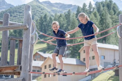 Ein Mädchen sitzt auf einem Klettergerüst auf dem Outdoor-Spielplatz des Familienhotels Gorfion in Liechtenstein.