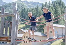 Ein Mädchen sitzt auf einem Klettergerüst auf dem Outdoor-Spielplatz des Familienhotels Gorfion in Liechtenstein.