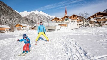 Vater und Kind fahren auf der Piste direkt vor dem Familienhotel Huber in Südtirol Ski