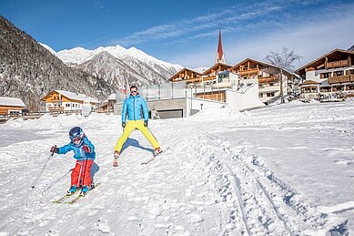 Vater und Kind fahren auf der Piste direkt vor dem Familienhotel Huber in Südtirol Ski