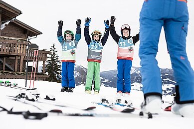 Drei Jungs stehen im Schnee und halten beim Skikurs vom Allgäuer Berghof die Hände in die Höhe.