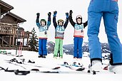 Drei Jungs stehen im Schnee und halten beim Skikurs vom Allgäuer Berghof die Hände in die Höhe.