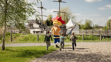 Drei Kinder laufen mit dem Hotel-Maskottchen Klausi zu dem großen Piratenschiff am Familienhotel Seeklause an der Ostsee