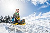 Kind fährt Schlitten am Familienhotel Landhaus zur Ohe im Bayerischen Wald.