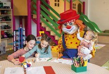Kinder malen in der liebevollen Kinderbetreuung des Familienhotels Alpenhotel Kindl in Tirol. Zu Besucht ist Clown Happy, das Maskottchen des Familienhotels.