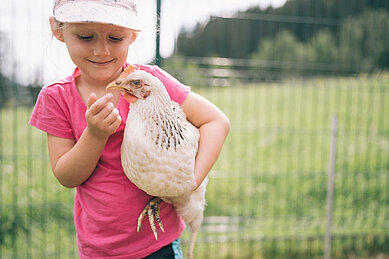 Kleines Mädchen hält eine Gans im Arm und füttert sie im Streichelzoo des Familienhotels Kirchheimerhof in Kärnten.