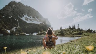 Eine Frau sitzt am See und genießt den Sommer im Allgäu. Der Tag ist schön und im Hintergrund steht ein Berg.