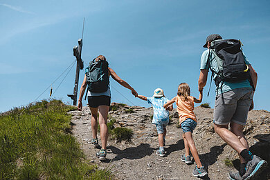 Familie mit zwei Kindern auf dem letzten Weg zum Gipfelkreuz im Wanderurlaub in Tirol.