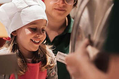 Kind steht mit Kochmütze auf dem Kopf am Buffet vom Familienhotel Tirolerhof